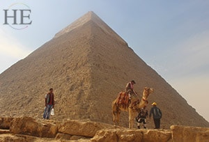 a man and his camel trotting in front of a great pyramid