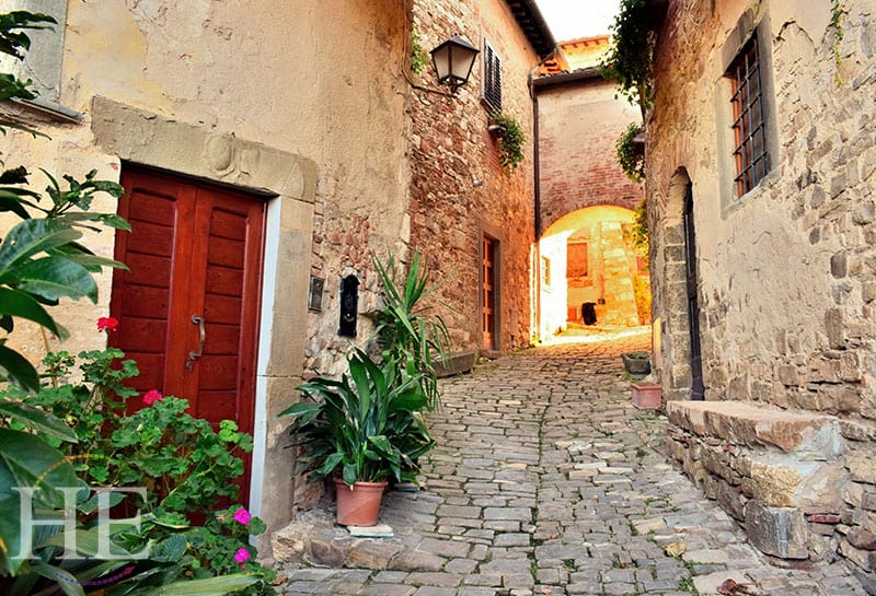beautiful red door peers from the corner of a historic village street in montefioralle
