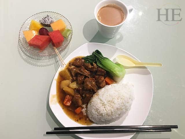 a meal of rice, beef, vegatables and fruit in an airport in china