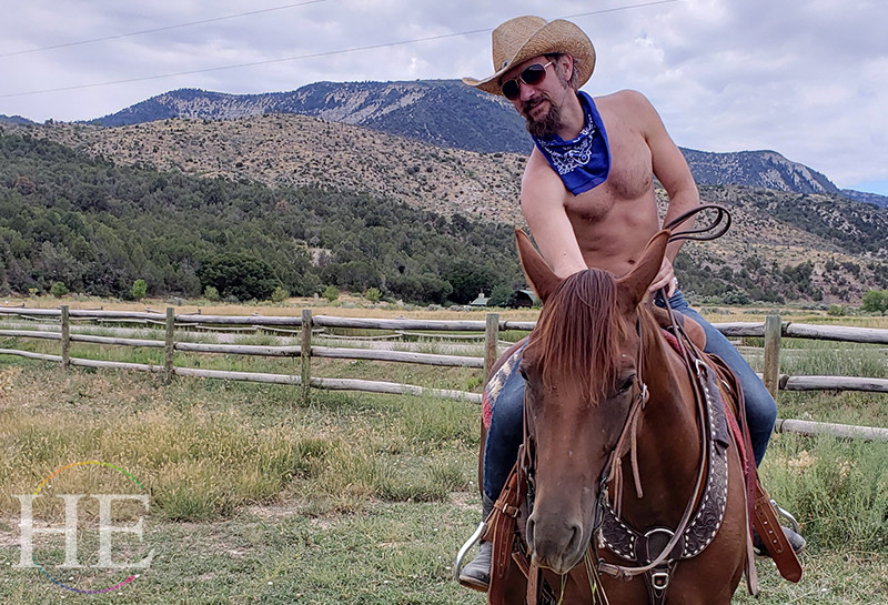 Zachary shirtless, riding a horse with mountains in the distance on HE Travel's Colorado Dude Ranch Tour.