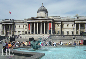 The front of the National Gallery Museum in London with people sitting around a fountain in the foreground on HE Travel's United Kingdom Town and Country Tour.