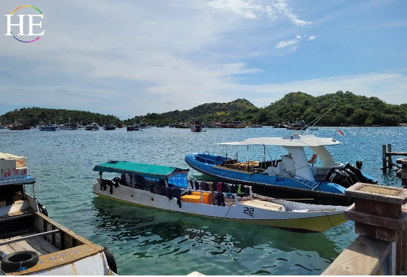 two boats in forground several in background. Blue water and green foliage of background island in Indonesia
