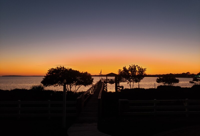 Sunset on cedar Key. Bright orange horizon leading to a dark blue sky. Trees are silhouetted in the forground.